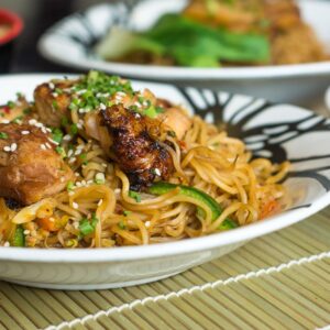 Close-up of delicious Asian-style noodles with grilled chicken and vegetables on a bamboo mat.