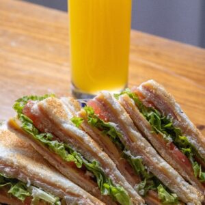 Close-up of a BLT sandwich with lettuce, tomato, and bacon served with orange juice.