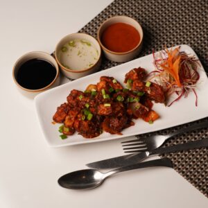 Plate of Asian-style crispy chicken with side sauces and garnished vegetables on a dining table.