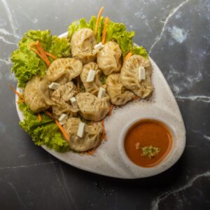 Tasty homemade paneer momos served with spicy chutney on a marble background.