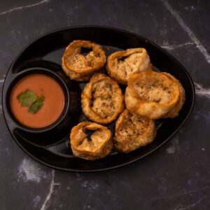 Delicious crispy cheese corn momos served with a spicy dipping sauce on a black plate.