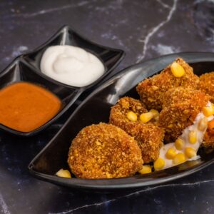 Delicious crispy cheese corn momos served with spicy and creamy sauces on a marble surface.