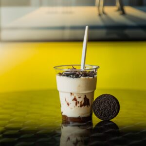 Creamy Oreo milkshake on a reflective surface with a yellow backdrop. Perfect sweet treat visual.