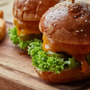 Close-up of juicy cheeseburgers with lettuce and pickles served on a wooden board.