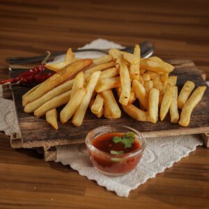 Golden French fries served on a rustic wooden board with spicy ketchup and chili pepper garnish, perfect for fast food lovers.