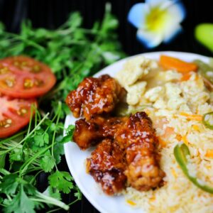 A vibrant Asian fusion dish with fried rice, glazed chicken, and fresh vegetables, garnished with cilantro.